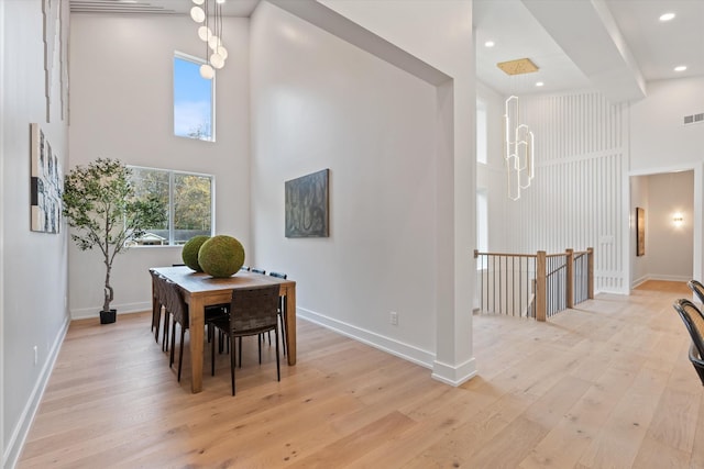 dining room with baseboards, visible vents, light wood-style flooring, and a high ceiling