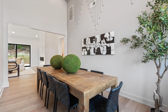 dining space with light wood finished floors, a high ceiling, and baseboards