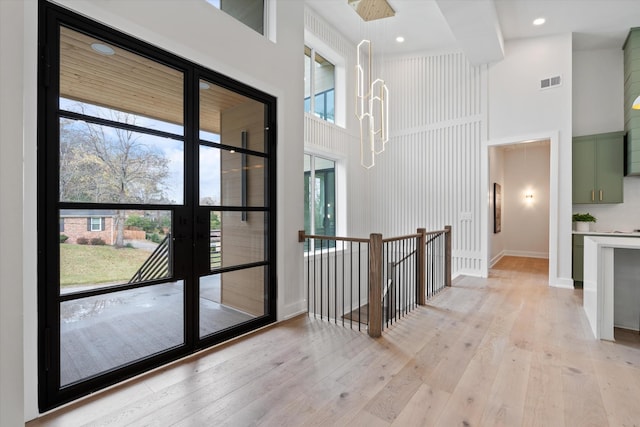 corridor featuring recessed lighting, a towering ceiling, baseboards, visible vents, and light wood finished floors