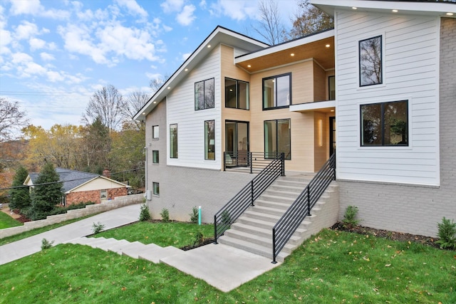 contemporary home featuring stairway, a front lawn, and brick siding