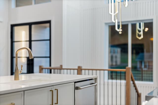 interior space with a sink, white cabinetry, light countertops, stainless steel dishwasher, and decorative light fixtures