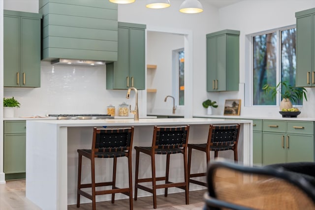 kitchen featuring green cabinetry, a kitchen breakfast bar, light countertops, light wood-style floors, and backsplash