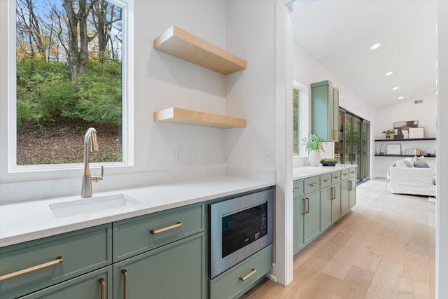 kitchen featuring light wood-style flooring, built in microwave, light countertops, open shelves, and a sink