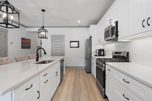 kitchen featuring light stone counters, stainless steel appliances, a sink, white cabinetry, and hanging light fixtures