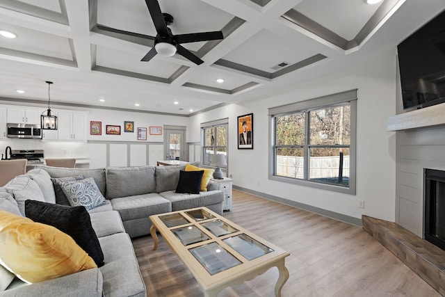 living room with visible vents, a large fireplace, light wood-type flooring, coffered ceiling, and beamed ceiling