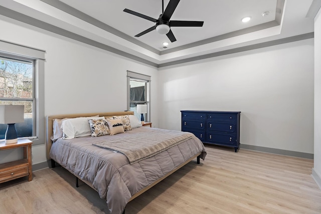 bedroom featuring light wood-type flooring, a raised ceiling, and baseboards