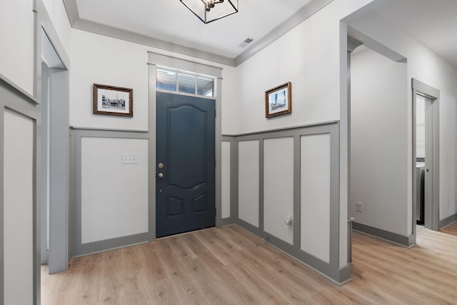 foyer entrance with visible vents, a decorative wall, and light wood finished floors