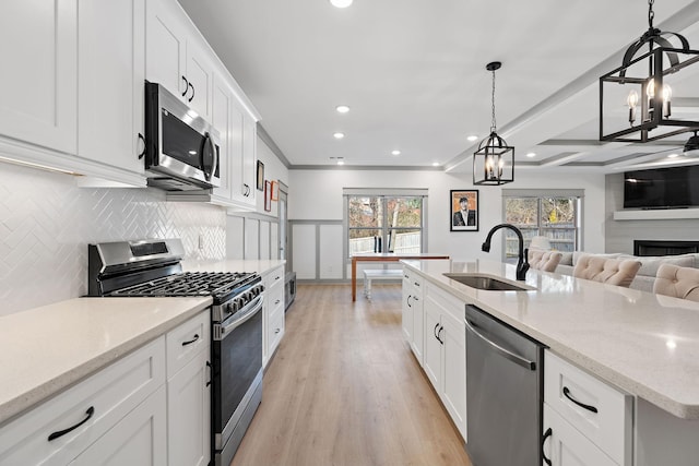 kitchen with stainless steel appliances, a sink, white cabinets, open floor plan, and pendant lighting