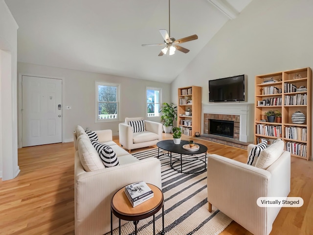 living area featuring a fireplace with raised hearth, ceiling fan, high vaulted ceiling, light wood-type flooring, and beamed ceiling