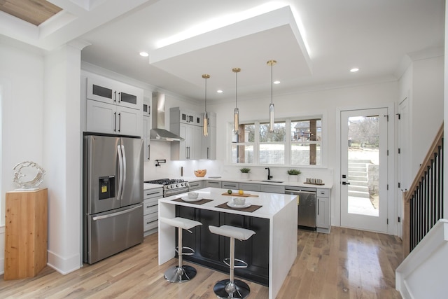 kitchen featuring stainless steel appliances, light countertops, wall chimney range hood, a center island, and glass insert cabinets