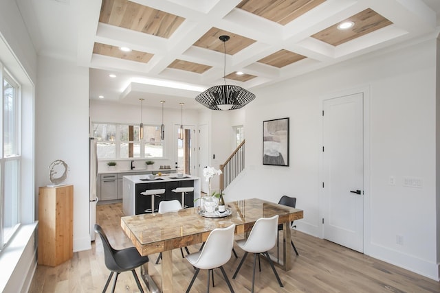 dining space with light wood-style flooring, baseboards, coffered ceiling, and beam ceiling