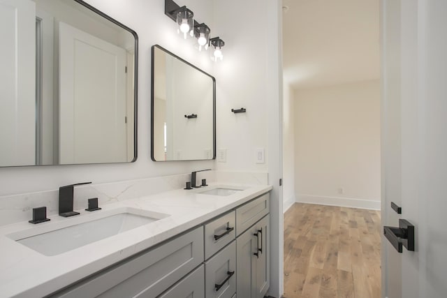 full bath featuring double vanity, wood finished floors, a sink, and baseboards