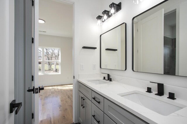 full bath featuring double vanity, wood finished floors, a sink, and baseboards