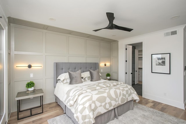 bedroom featuring light wood-style floors, visible vents, a decorative wall, and a ceiling fan