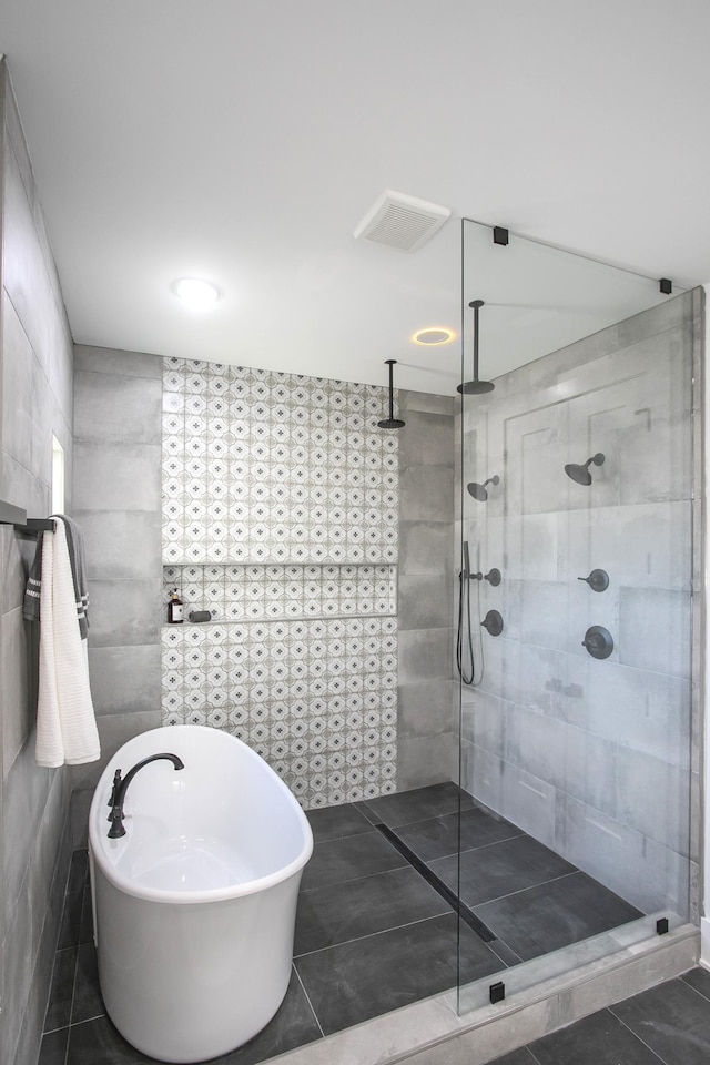 full bath featuring visible vents, tile patterned flooring, walk in shower, a freestanding bath, and tile walls