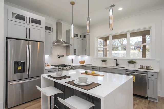 kitchen featuring appliances with stainless steel finishes, glass insert cabinets, a kitchen island, light stone countertops, and wall chimney exhaust hood