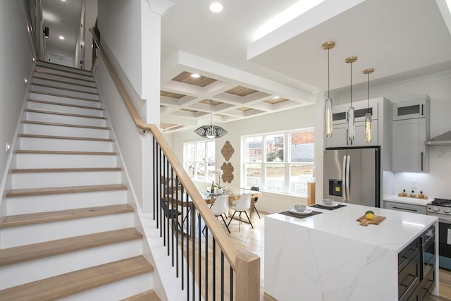 kitchen featuring stainless steel appliances, coffered ceiling, hanging light fixtures, and beamed ceiling