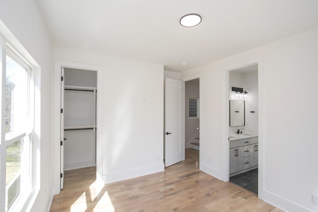 unfurnished bedroom featuring baseboards, a sink, a walk in closet, and light wood-style floors