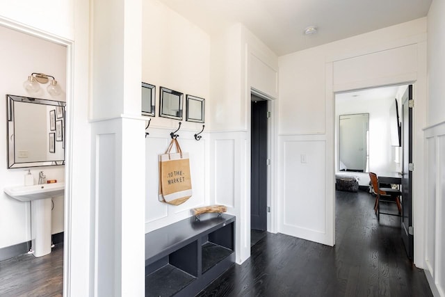 mudroom with dark wood-style flooring, wainscoting, a decorative wall, and a sink