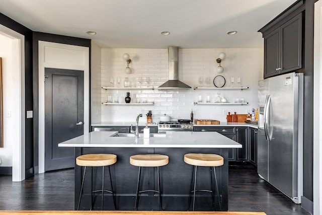 kitchen featuring open shelves, appliances with stainless steel finishes, wall chimney exhaust hood, and a kitchen island with sink