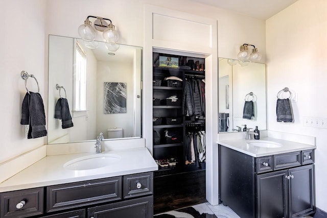 bathroom with toilet, a spacious closet, two vanities, and a sink