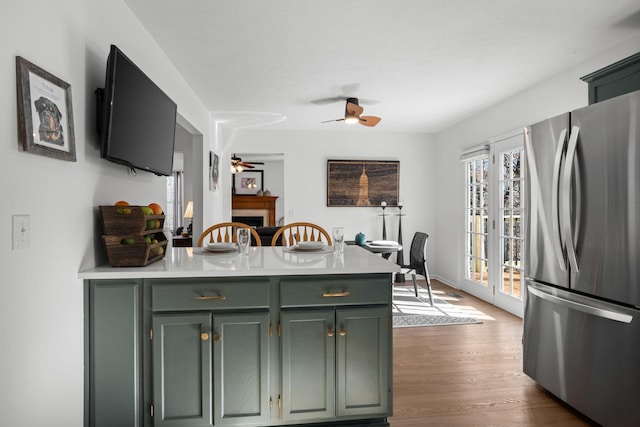 kitchen with dark wood-style flooring, a fireplace, a ceiling fan, light countertops, and freestanding refrigerator