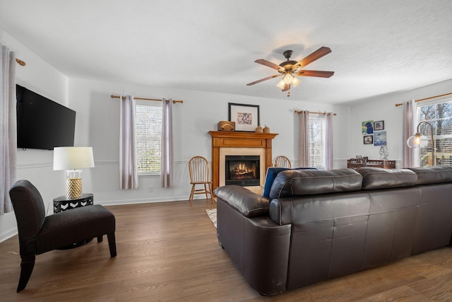 living room with a warm lit fireplace, baseboards, dark wood-style floors, and a wealth of natural light