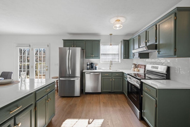 kitchen featuring appliances with stainless steel finishes, light countertops, under cabinet range hood, green cabinets, and a sink