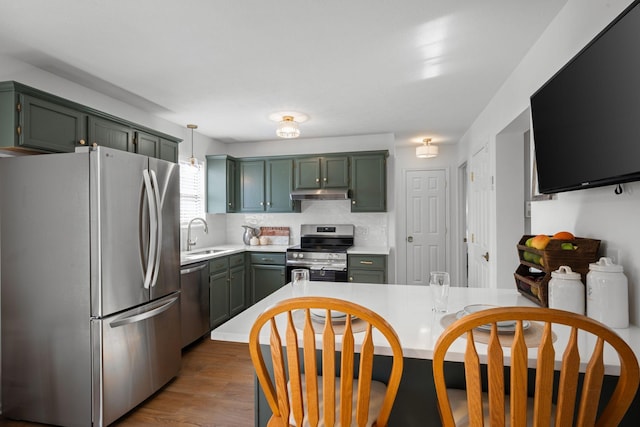 kitchen with under cabinet range hood, wood finished floors, a sink, light countertops, and appliances with stainless steel finishes