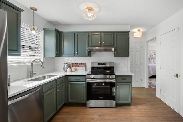 kitchen with stainless steel appliances, a sink, light countertops, decorative light fixtures, and green cabinetry