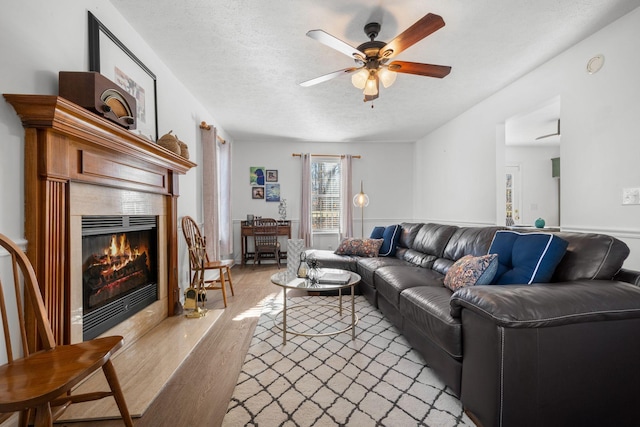 living area featuring light wood finished floors, ceiling fan, a tiled fireplace, and a textured ceiling