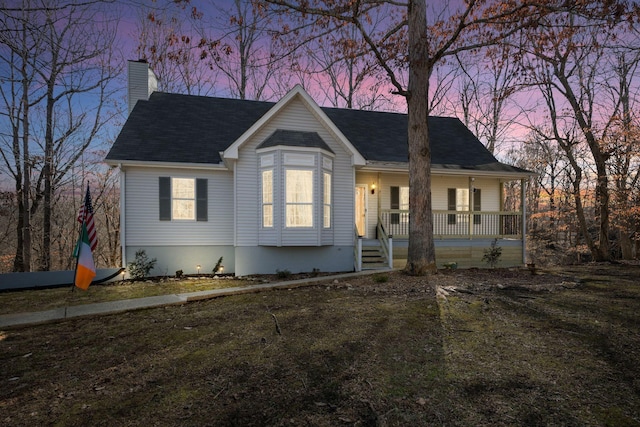 view of front of property featuring a shingled roof, a chimney, a porch, and a yard