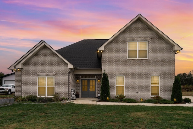 traditional home featuring a shingled roof, a front yard, french doors, and brick siding