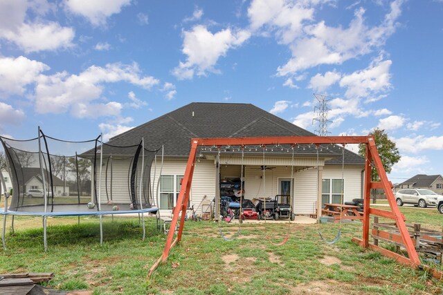 rear view of property with a trampoline, a yard, a patio, and roof with shingles