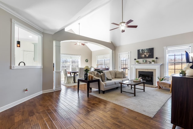 living area with a ceiling fan, arched walkways, dark wood finished floors, and a tiled fireplace