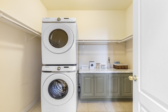 washroom with light tile patterned floors, stacked washer / dryer, cabinet space, and baseboards