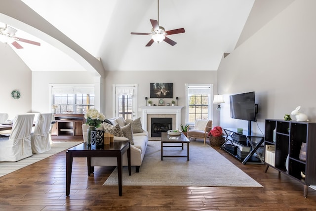 living area featuring arched walkways, a tiled fireplace, a ceiling fan, wood finished floors, and high vaulted ceiling