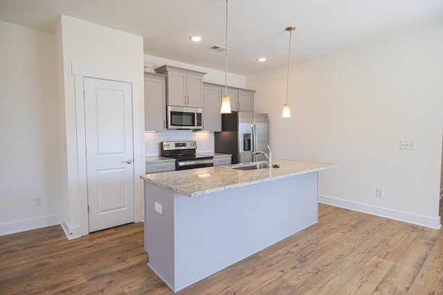 kitchen featuring appliances with stainless steel finishes, a sink, a center island with sink, and light stone countertops