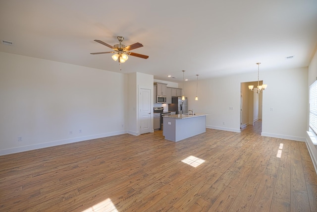 unfurnished living room with light wood finished floors, visible vents, baseboards, a sink, and ceiling fan with notable chandelier