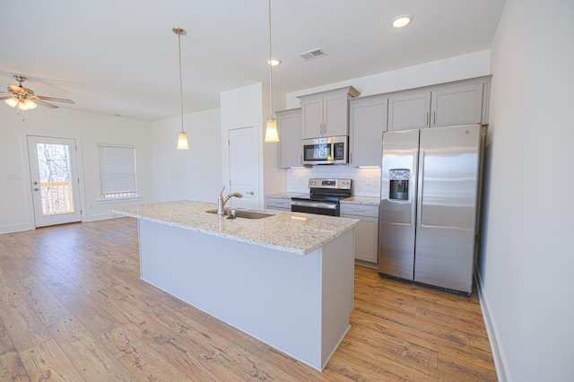 kitchen featuring stainless steel appliances, a center island with sink, visible vents, and light stone countertops