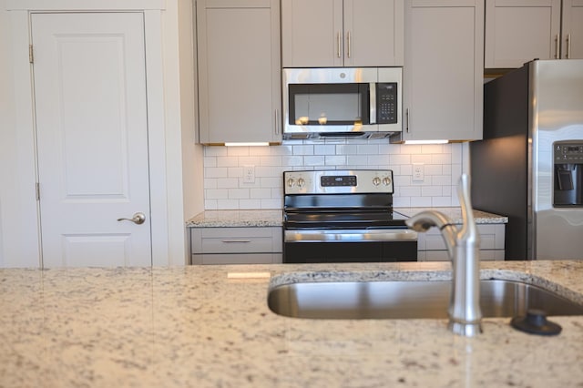 kitchen with gray cabinetry, stainless steel appliances, tasteful backsplash, and light stone countertops