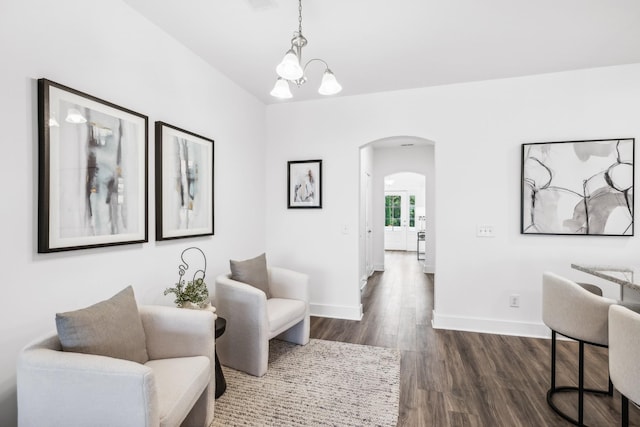 living area featuring dark wood-type flooring, arched walkways, a notable chandelier, and baseboards