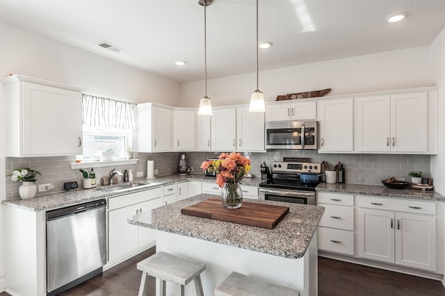 kitchen with stainless steel appliances, a sink, decorative light fixtures, and white cabinets