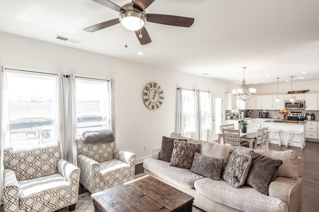 living area with a healthy amount of sunlight, baseboards, visible vents, and ceiling fan with notable chandelier