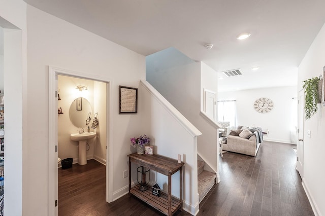 hallway with stairs, dark wood-type flooring, visible vents, and baseboards