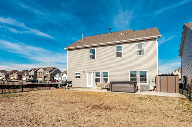 rear view of house with a hot tub, a fenced backyard, a storage unit, an outdoor structure, and a patio area