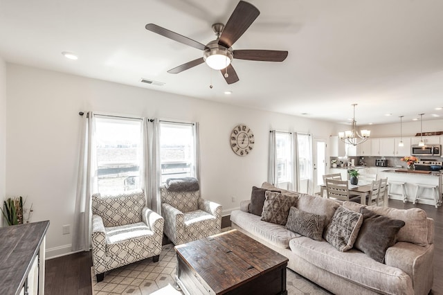 living area featuring baseboards, visible vents, wood finished floors, and ceiling fan with notable chandelier