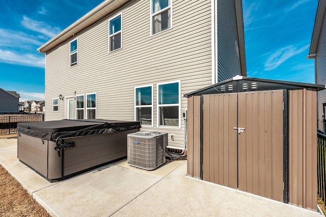 rear view of property featuring a storage shed, a hot tub, central AC unit, an outbuilding, and a patio area