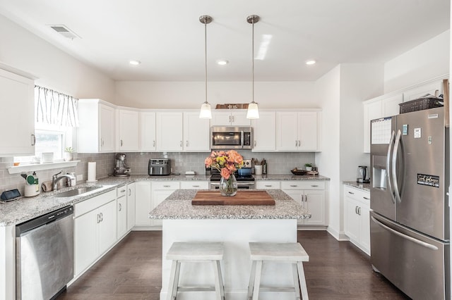 kitchen featuring a sink, white cabinets, hanging light fixtures, appliances with stainless steel finishes, and a center island