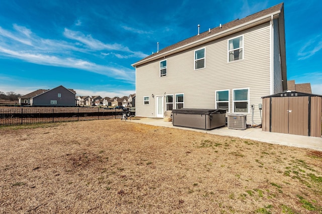 rear view of property with a storage shed, fence, a yard, a patio area, and a hot tub